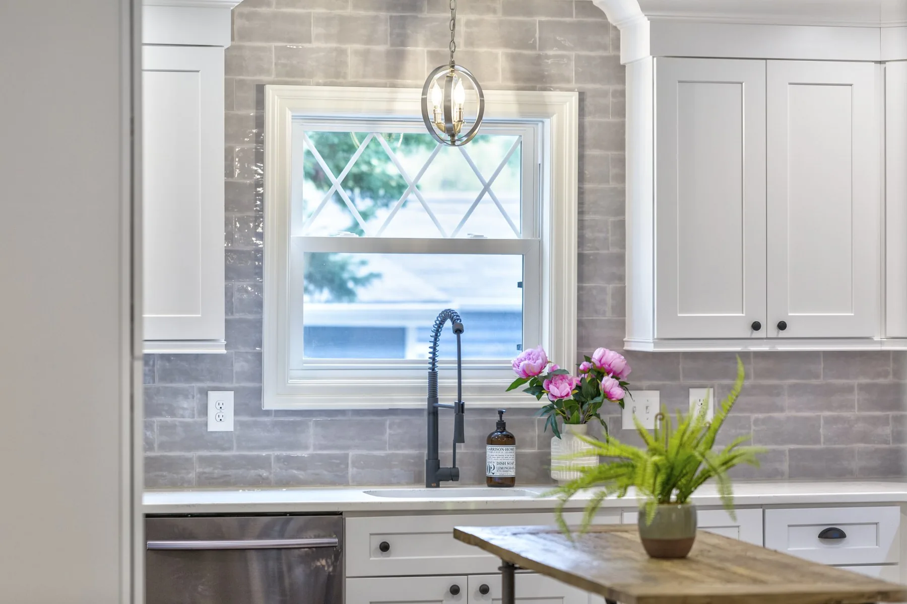 A bright kitchen with a farmhouse sink, grey tile and peonies on the counter